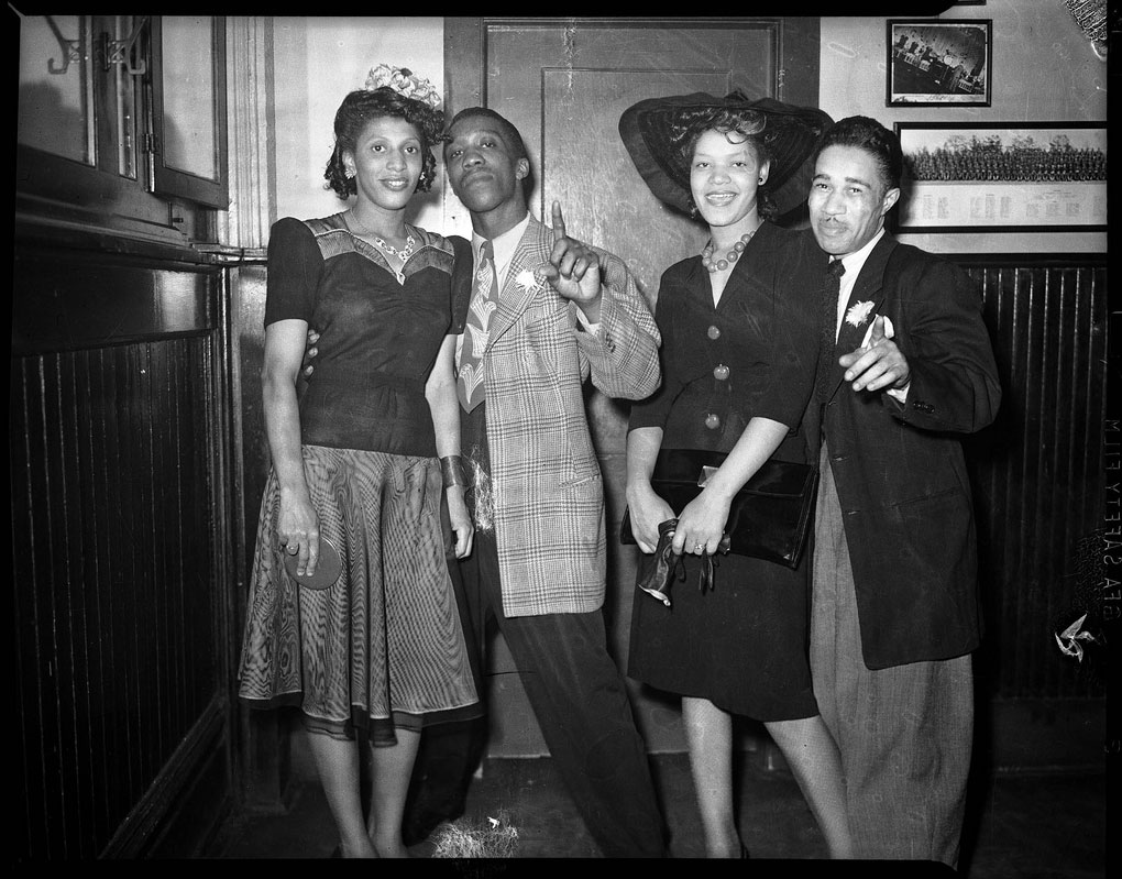 teenie-harris-group-portrait-of-two-women-and-two-men-woman-on-right-wearing-dark-dress-with-wide-brimmed-hat-in-interior-with-wainscoting-and-pictures-on-wall-c-1940-1945.jpg