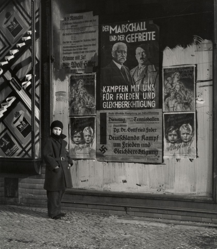 Roman Vishniac. '[Vishniac's daughter Mara posing in front of an election poster for Hindenburg and Hitler that reads "The Marshal and the Corporal: Fight with Us for Peace and Equal Rights," Wilmersdorf, Berlin]' 1933