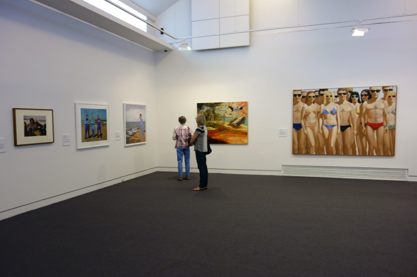 Installation view of the exhibition 'On the beach' at the Mornington Peninsula Regional Art Gallery showing at second left, Anne Zahalka's 'The girls #2, Cronulla Beach' (2007); at left on the far wall John Anderson's 'Abundance' (2015) followed by John Hopkins 'The crowd' (1970)