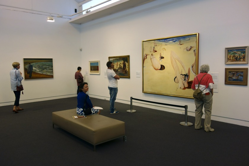 Installation view of the exhibition 'On the beach' at the Mornington Peninsula Regional Art Gallery showing in the centre, Brett Whiteley's 'Balmoral' (1975-1978). To the left of this painting is Nancy Kilgour's 'Figures on Manly Beach' (1930) and to the right Norma Bull's 'Bathing Beach' (c. 1950-1960s) with at bottom, George W. Lambert's 'Anzacs bathing in the sea' (1915)