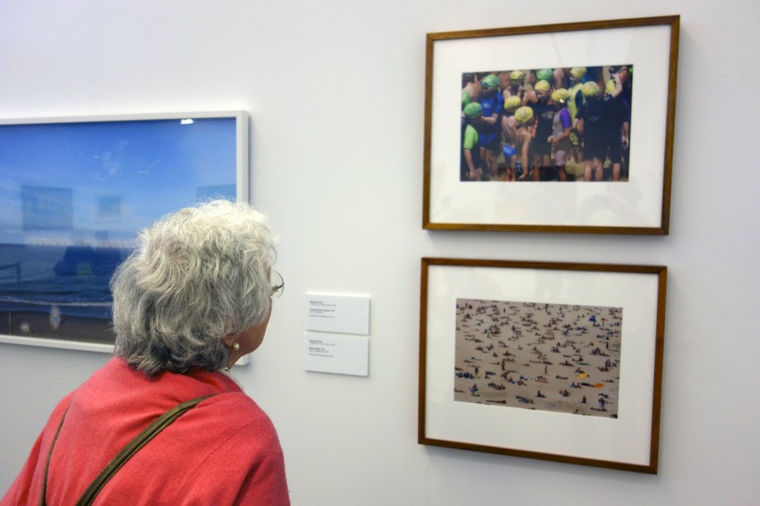 Photographer Joyce Evans looking at two colour photographs by Rennie Ellis in the exhibition 'On the beach' at the Mornington Peninsula Regional Art Gallery