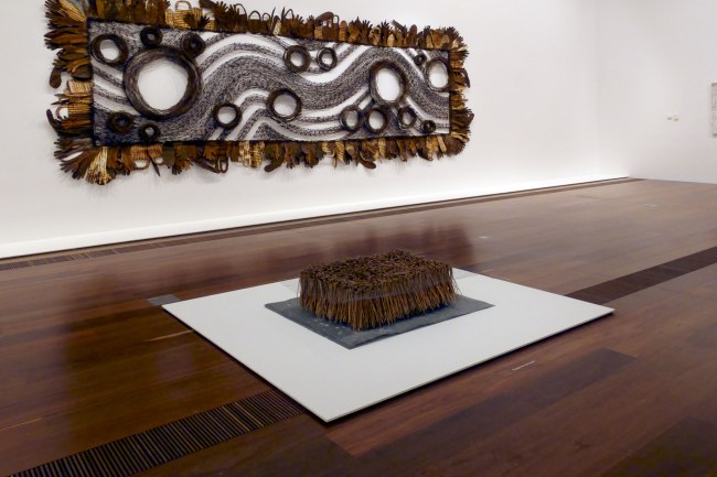 Installation view of Rosalie Gascoigne's 'Crop 2' (1982, foreground) and Lorraine Connelly-Northey's 'A Possum Skin cloak: Blackfella road' (2011-2013, background) at the exhibition 'Found and Gathered' at The Ian Potter Centre NGV Australia