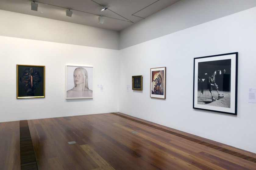 Installation view of the exhibition 'WHO ARE YOU: Australian Portraiture' at NGV Australia, Federation Square, Melbourne showing at second left, Petrina Hicks' 'Lauren' (2003); at third right, Christian Waller's 'Destiny' (1916); at second right, Charles Dennington's 'Adut Akech' (2018); and at right, Tony Kearney's 'Gill Hicks' (2016)