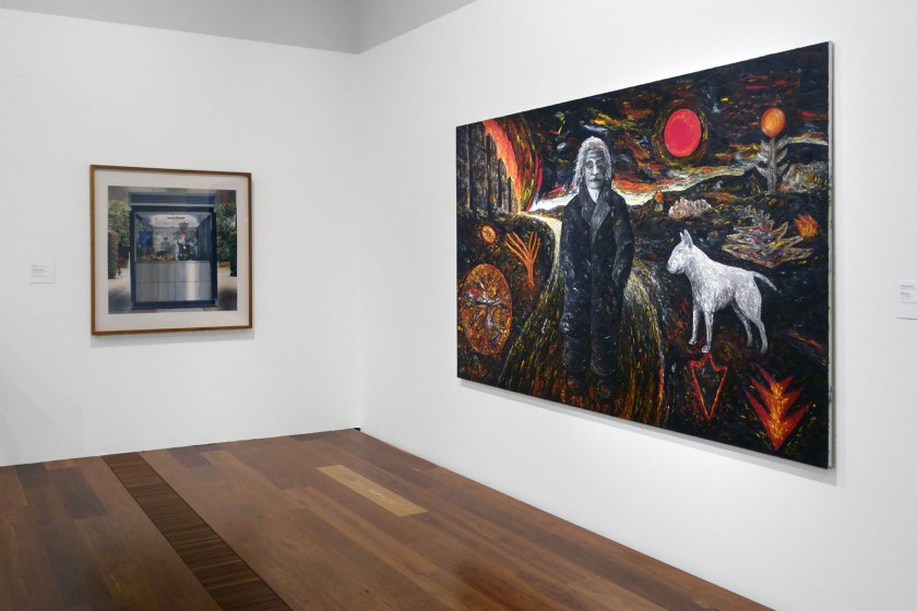 Installation view of the exhibition 'WHO ARE YOU: Australian Portraiture' at NGV Australia, Federation Square, Melbourne showing at left, Selina Ou's 'Anita ticket seller' (2002); and at right, Peter Booth's 'Painting' (1977)