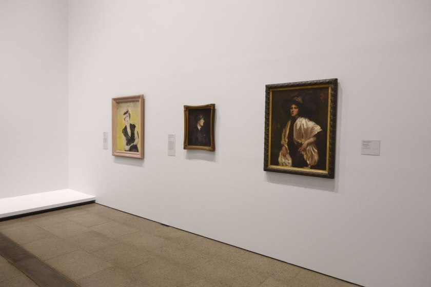 Installation view of the exhibition 'WHO ARE YOU: Australian Portraiture' at NGV Australia, Federation Square, Melbourne showing at left, Lina Bryans' 'The babe is wise' (1940); at middle, Janet Cumbrae Stewart's 'Portrait of Jessie C. A. Traill' (1920); and at right, Evelyn Chapman's 'Self portrait' (1911)