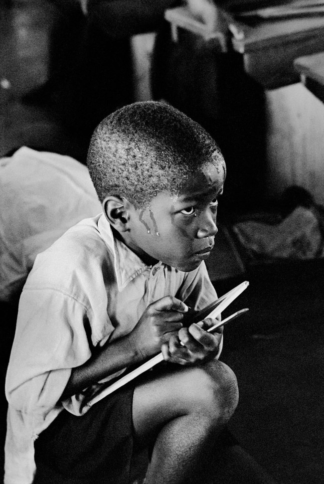 Ernest Cole (South African, 1940-1990) 'Earnest boy squats on haunches and strains to follow lesson in heat of packed classroom, South Africa' 1960-1966