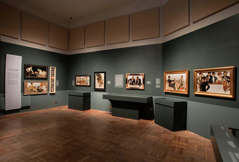 Installation view of the exhibition 'Under Cover: J.C. Leyendecker and American Masculinity' at the New-York Historical Society showing at left top, 'Men Reading' (1914) and at left bottom, 'Men with Golf Clubs' (c. 1909); at centre, 'The Donchester – the Cluett Dress Shirt' (1911); and at right, 'In the Stands 2' (1913)