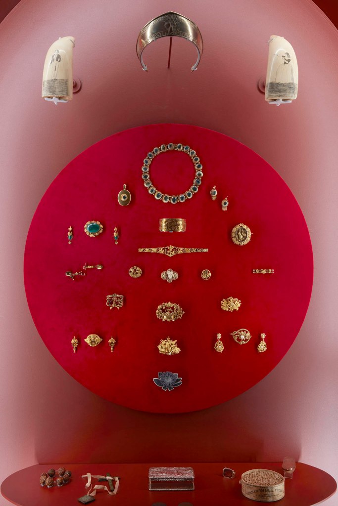 Installation view of the exhibition '1,001 Remarkable Objects' at Powerhouse Ultimo, Sydney showing examples of 19th century Australian gold jewellery in the Powerhouse Collection including at top, a parure comprising necklace, locket and earrings (pair), gold / operculum by F Allerding & Son, Sydney, New South Wales, Australia, 1879-1884; and at second top centre, Bangle, 'Soyons toujours unis / Par un divin amour', 18 carat gold, Henry Steiner, Adelaide, South Australia, c. 1878